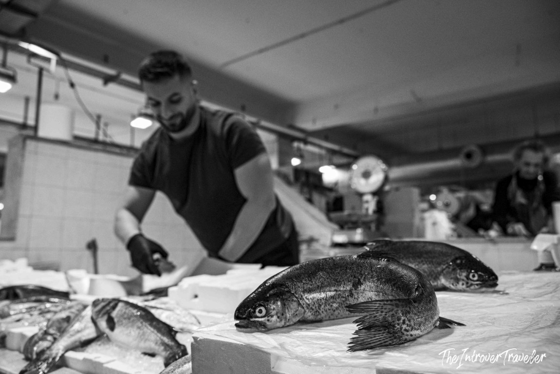 Fishmonger preparing fresh whole fish at a bustling indoor coastal city fish market