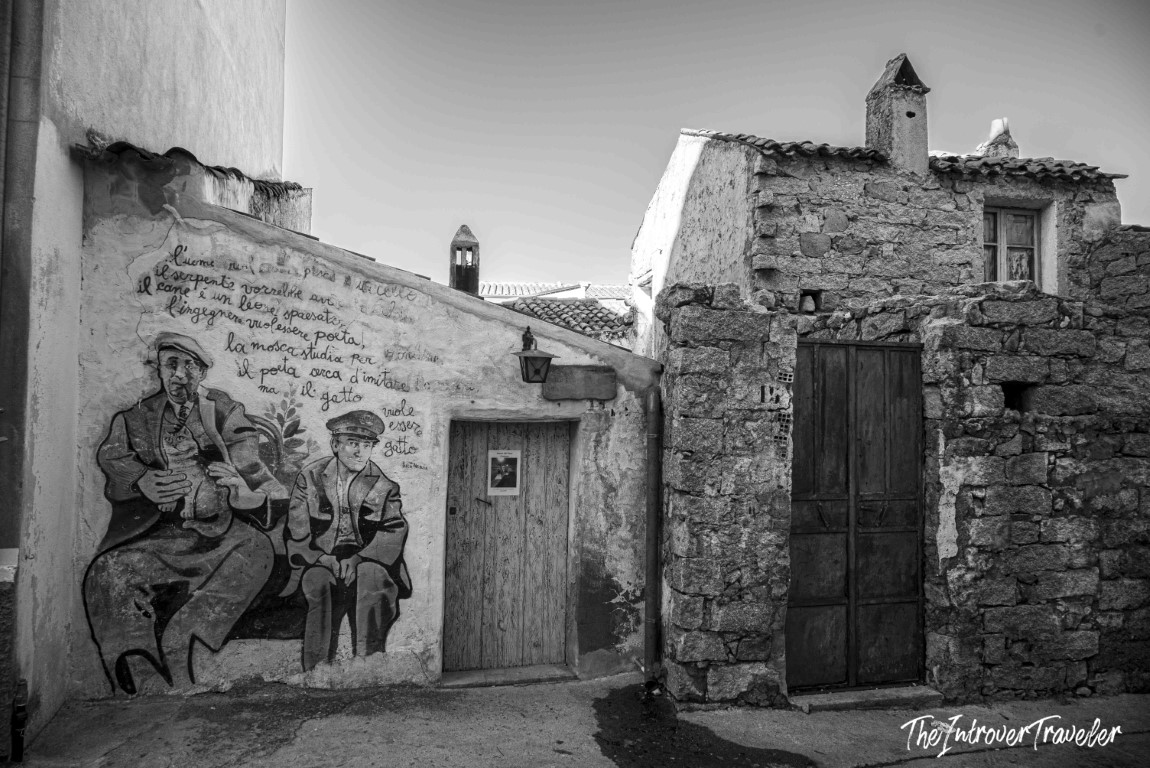 Street mural with Italian verse and two seated figures on a stone building in Orgosolo, Sardinia