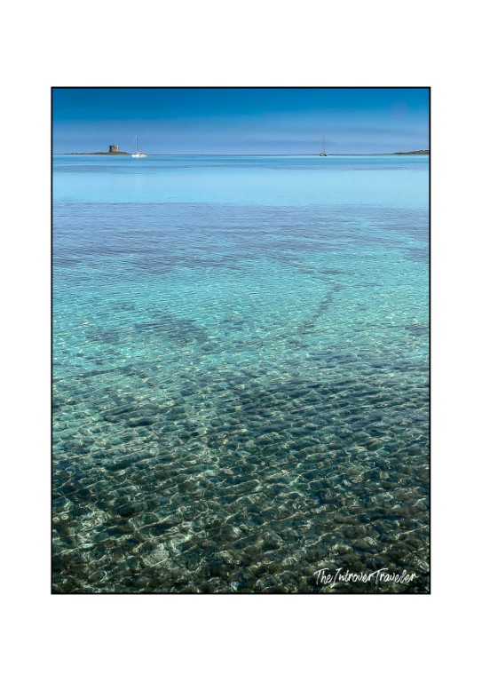 Crystal-clear turquoise shallows at La Pelosa Beach, Stintino, with the medieval Torre della Pelosa in the distance