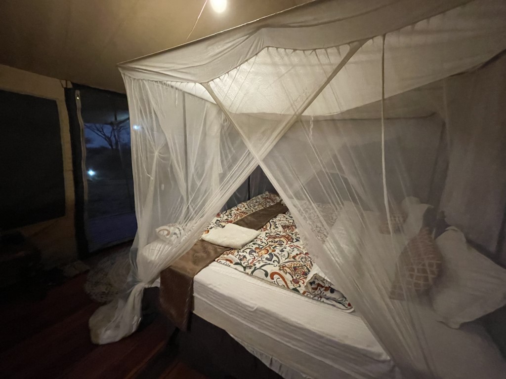 Mosquito net canopy bed inside a Tanzania safari glamping tent at night