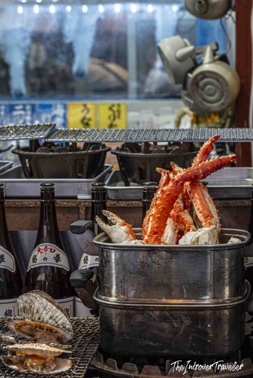 King crab legs steaming in a pot at Tsukiji fish market Tokyo, with scallops and sake bottles nearby