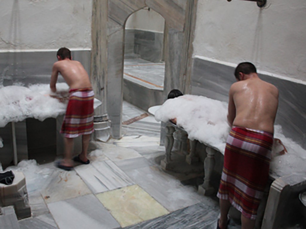 Visitors wrapped in red pestemals receiving foam massage at Süleymaniye Hamam marble basins, Istanbul