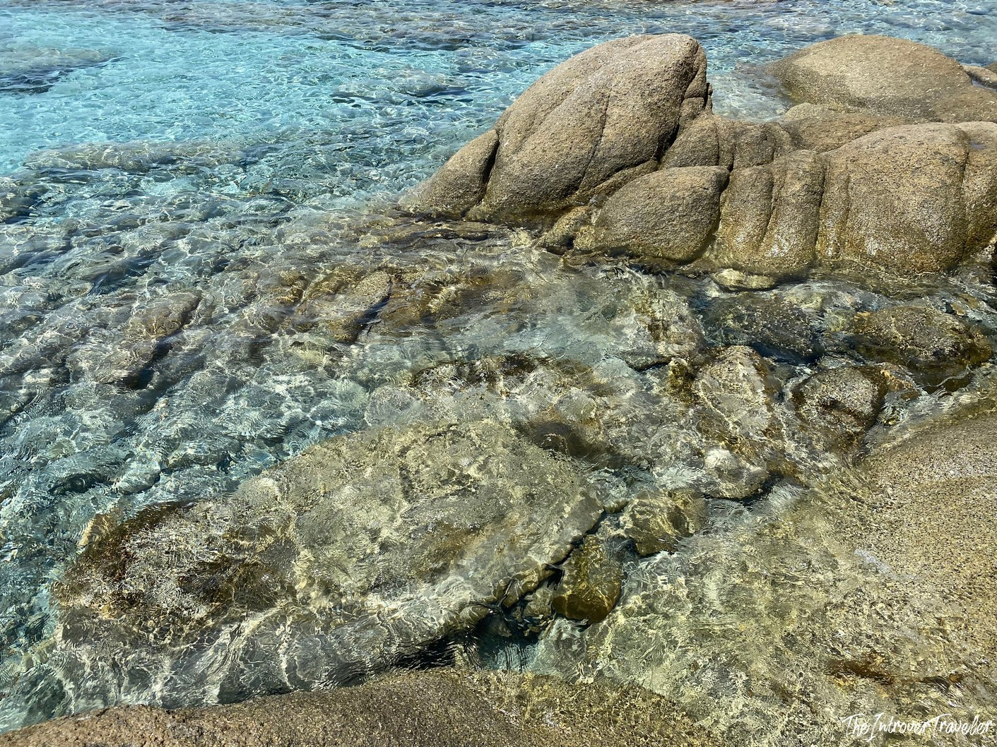 Crystal-clear turquoise water lapping over granite rocks on a south Sardinia beach shore