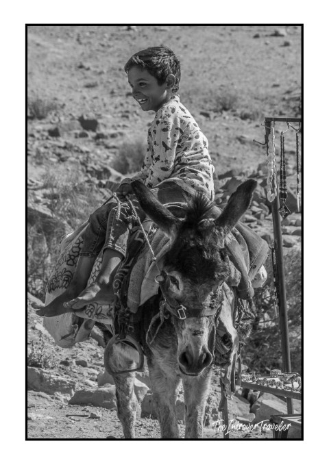 Smiling Jordanian boy riding a donkey near the rocky landscape of Petra, Jordan