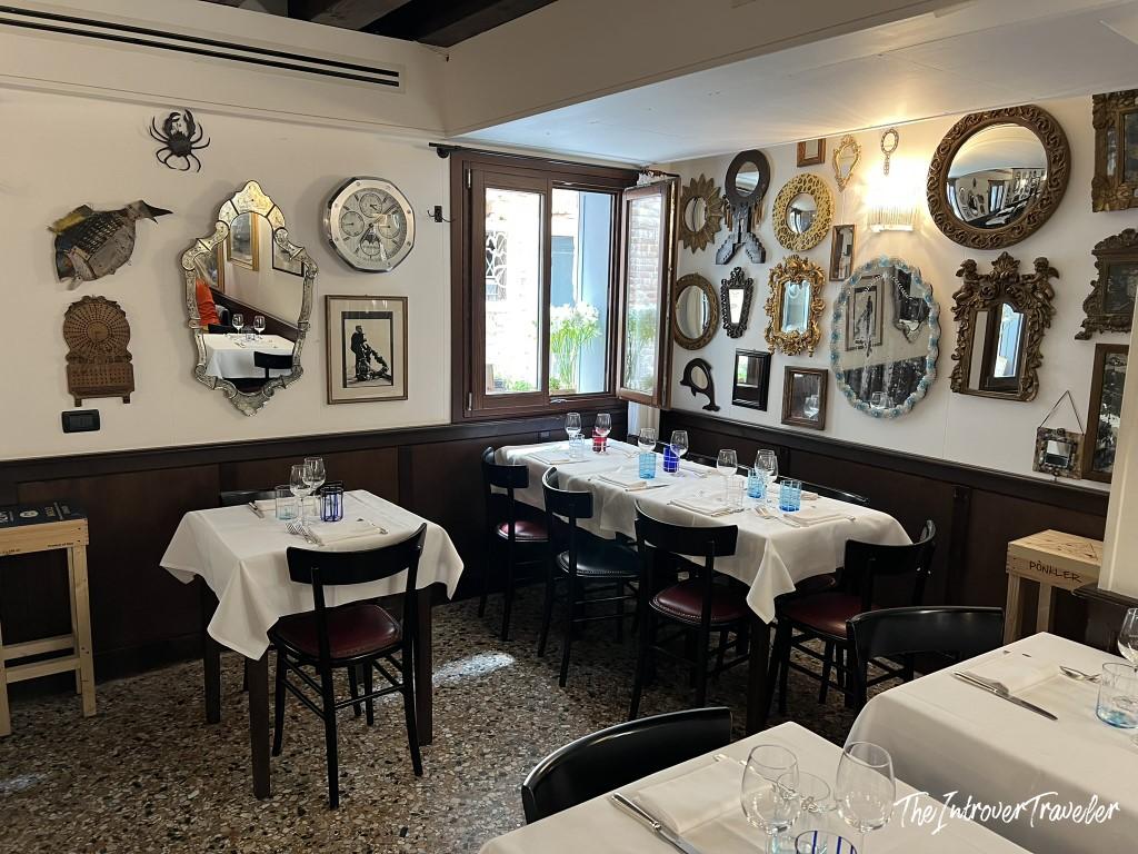 Cozy dining room at Le Antiche Carampane Venice, with Murano mirrors, set white-linen tables, and terrazzo floors