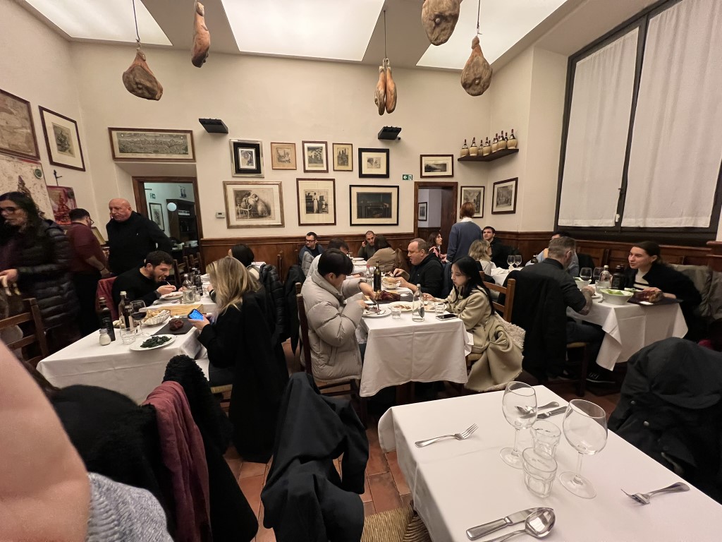 Busy dining room at Trattoria Il Latini Florence, with whole prosciutto hanging from the ceiling