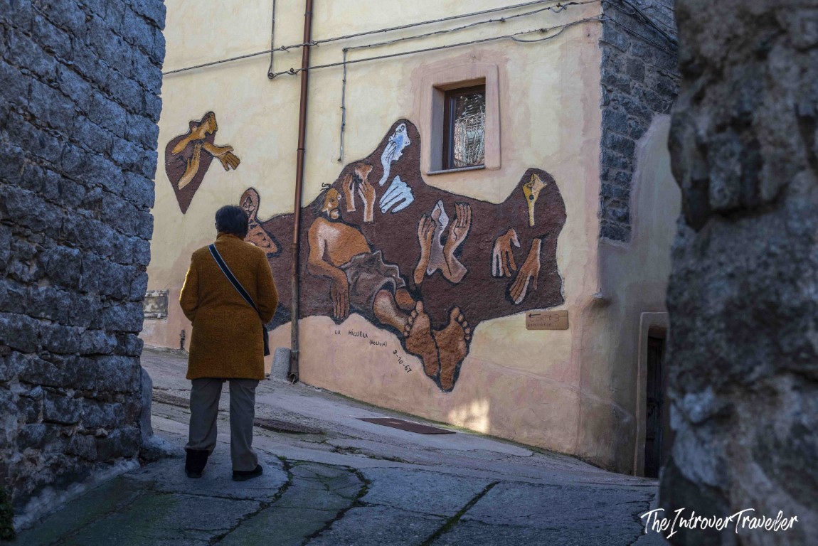 Visitor admiring a mural in Orgosolo referencing La Higuera Bolivia, October 1967, on a village wall