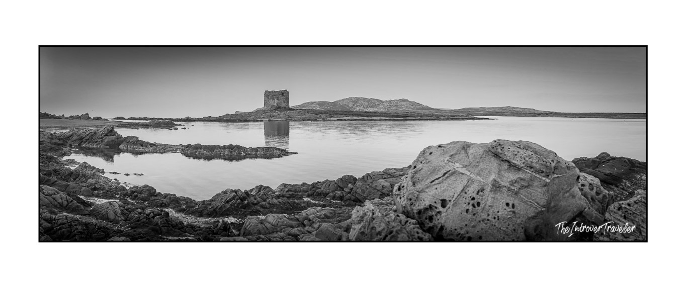 Black and white panorama of Torre della Pelosa reflected in calm waters at La Pelosa Beach, Stintino