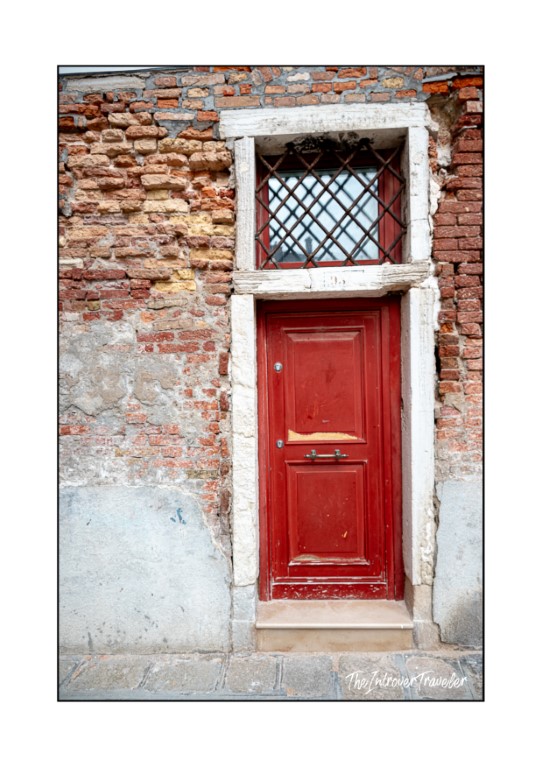 Weathered red door with latticed transom window on a rustic brick building in Venice