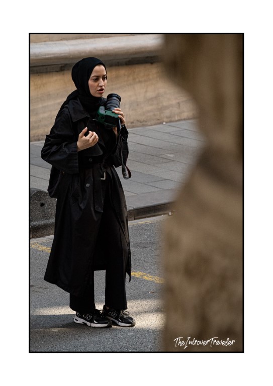 Woman in black hijab and coat photographing Istanbul streets with a DSLR camera