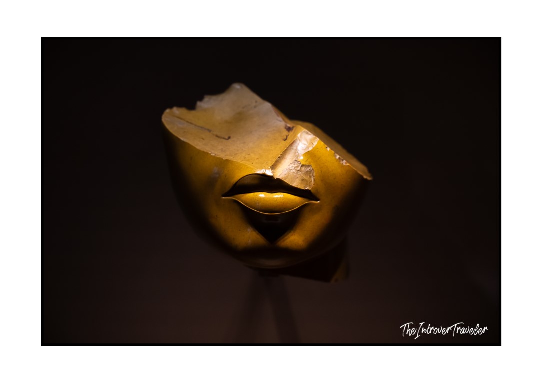 Golden gilded fragment of an ancient female face sculpture, showing only lips and chin, at the Met