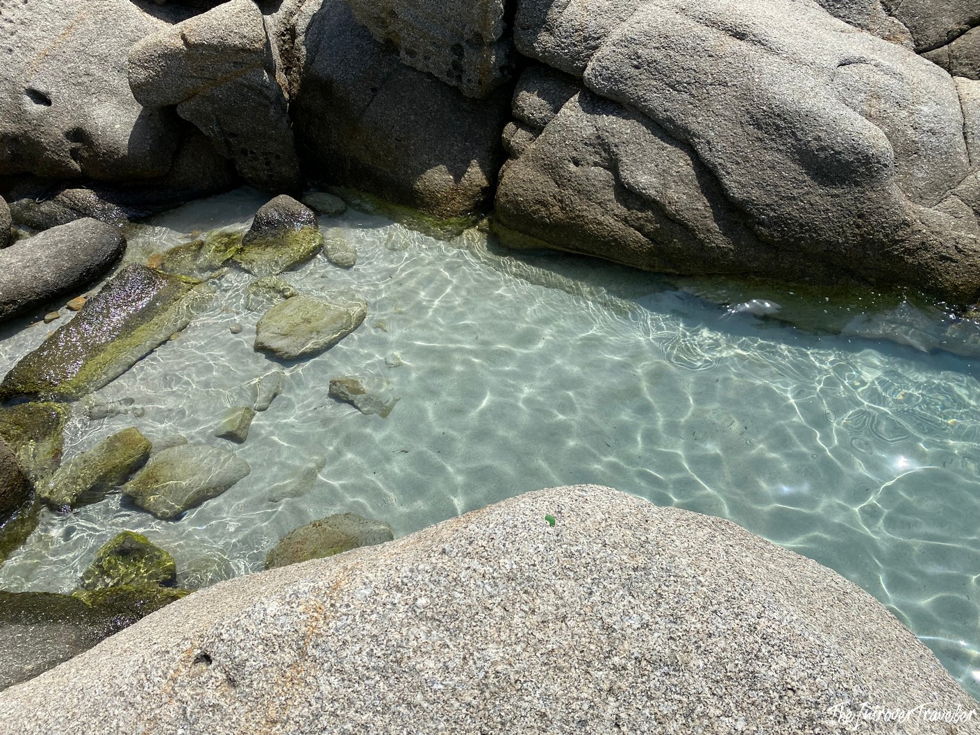 Crystal clear tidal pool nestled between granite boulders on a south Sardinia beach