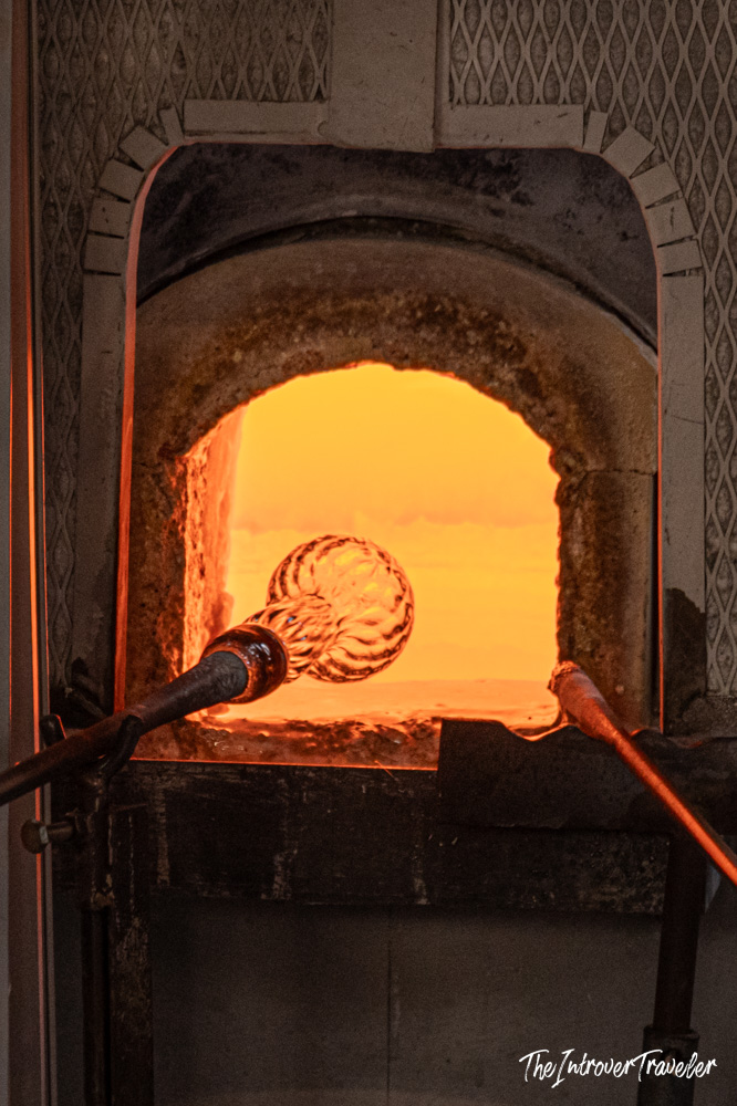 Murano glassblowing blowpipe with molten glass orb reheating inside a glowing furnace kiln