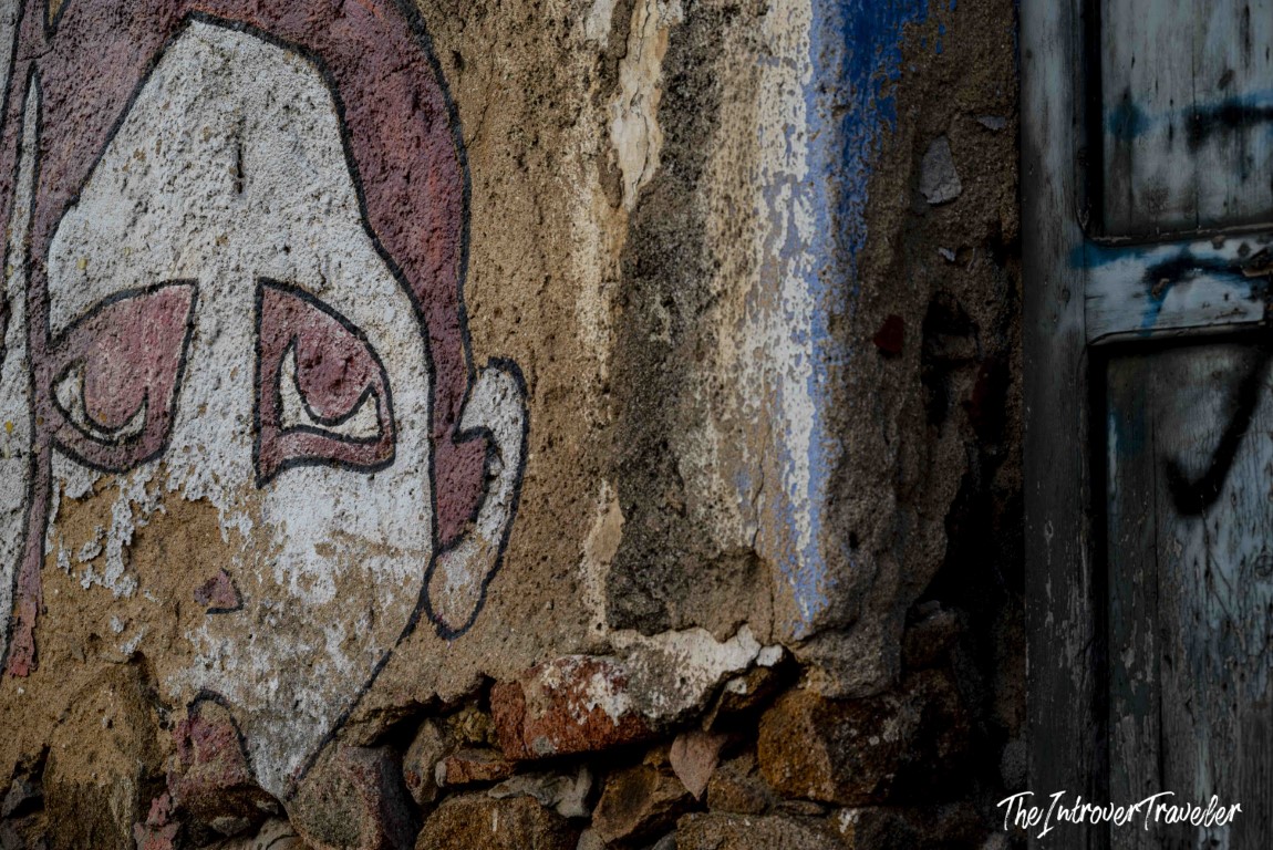 Close-up of a weathered, peeling mural on a crumbling stone wall in Orgosolo, Sardinia