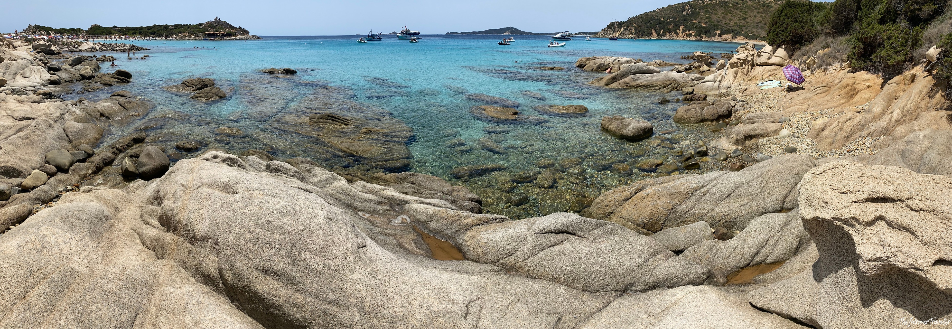 Granite rocks framing a crystal-clear turquoise cove in south Sardinia, with boats anchored in the bay