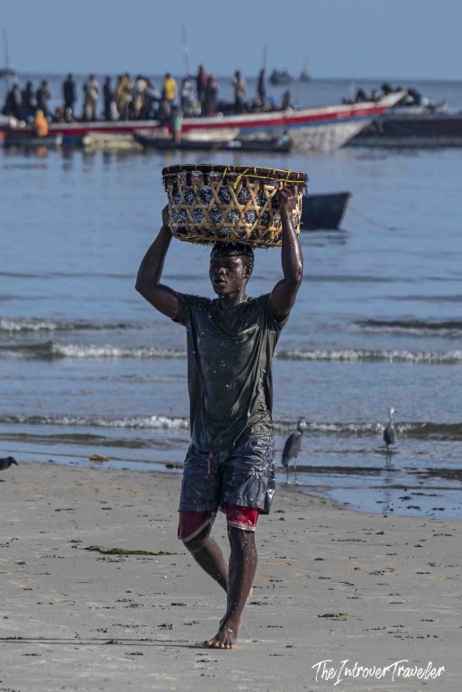 Fisherman carrying woven basket of catch on his head at a busy coastal fish market beach