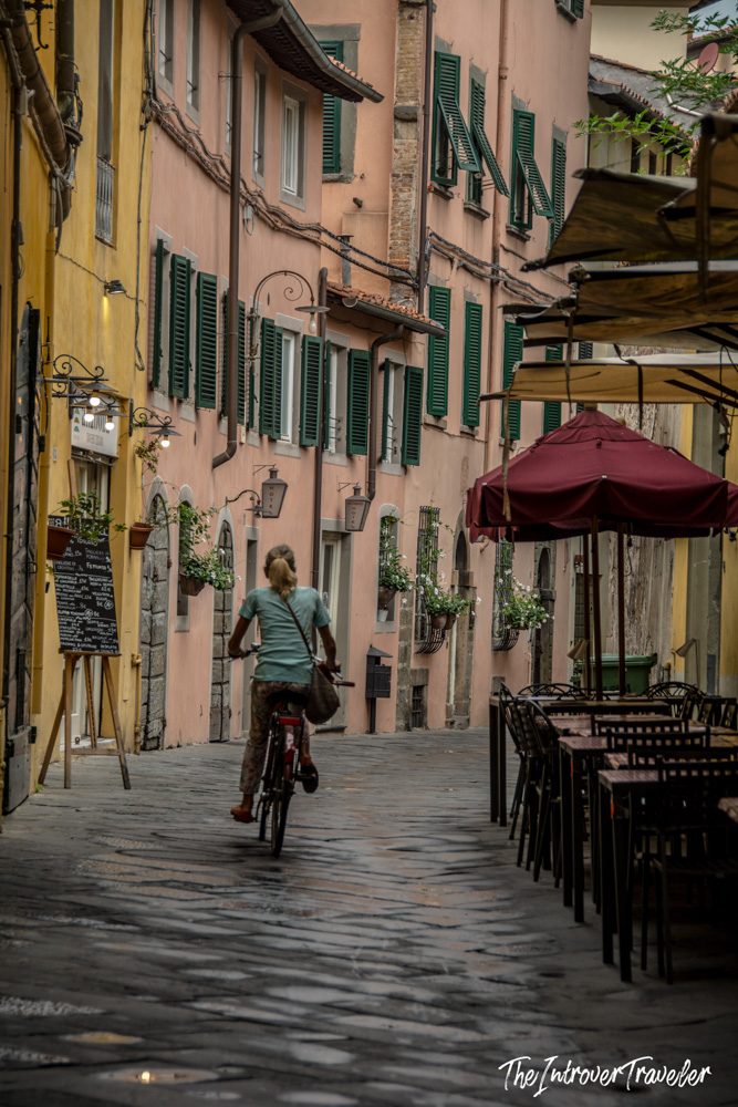 Cyclist riding through a narrow cobblestone alley in Lucca's historic old town, Tuscany