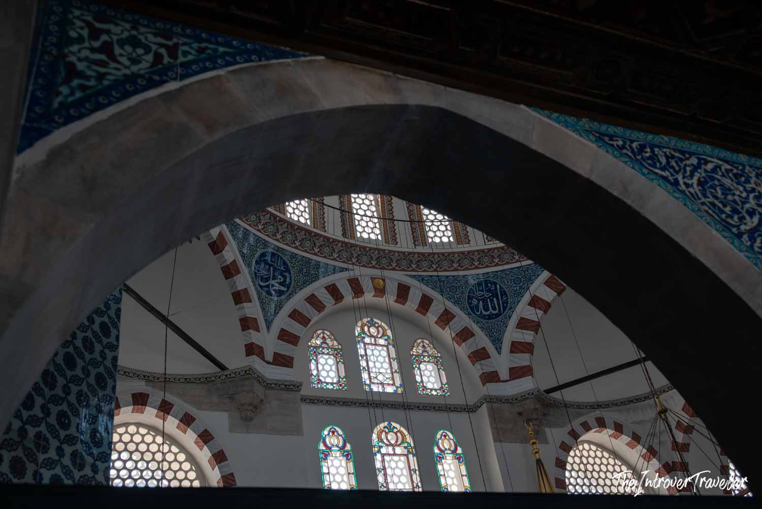 Interior dome and Iznik tile arches of a historic Istanbul mosque, with stained glass windows and Arabic calligraphy