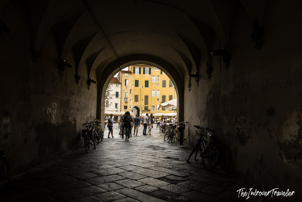Arched tunnel entrance to Piazza dell'Anfiteatro in Lucca, Tuscany, with cyclists and visitors