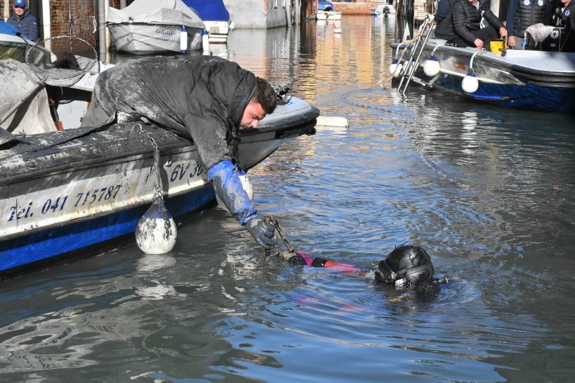 Diver and crew member recovering debris from a Venice canal during a cleanup operation