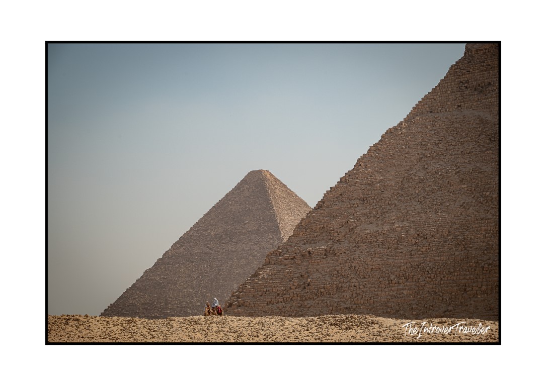 Camel rider dwarfed by the Pyramids of Giza, highlighting the colossal scale of the ancient monuments