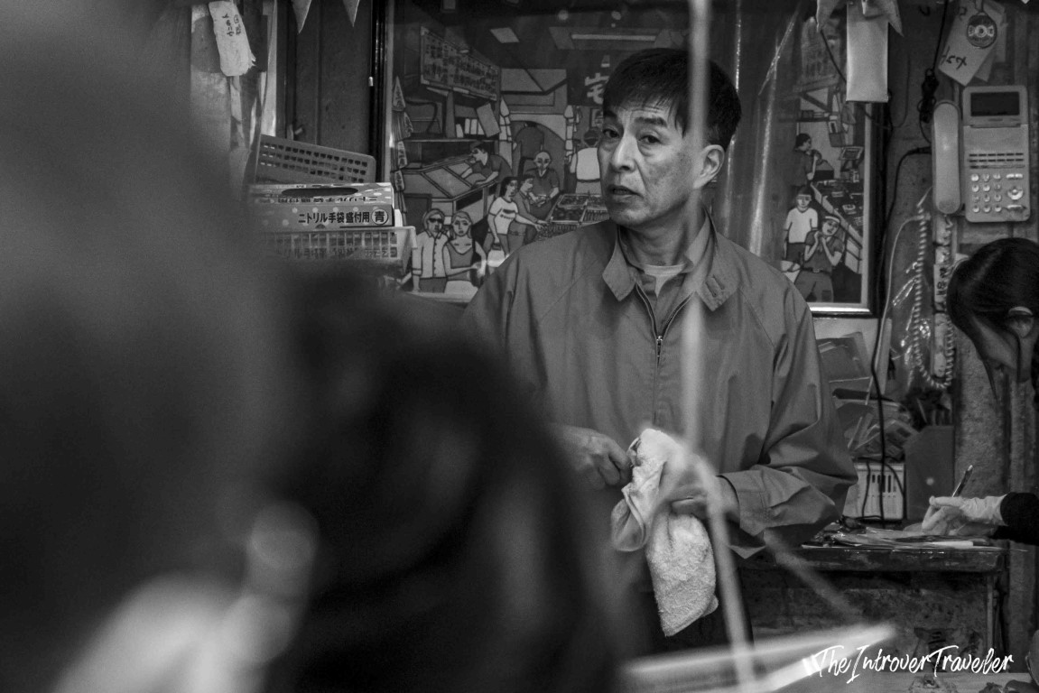 Tsukiji market vendor holding a cloth towel inside a cluttered Japanese stall