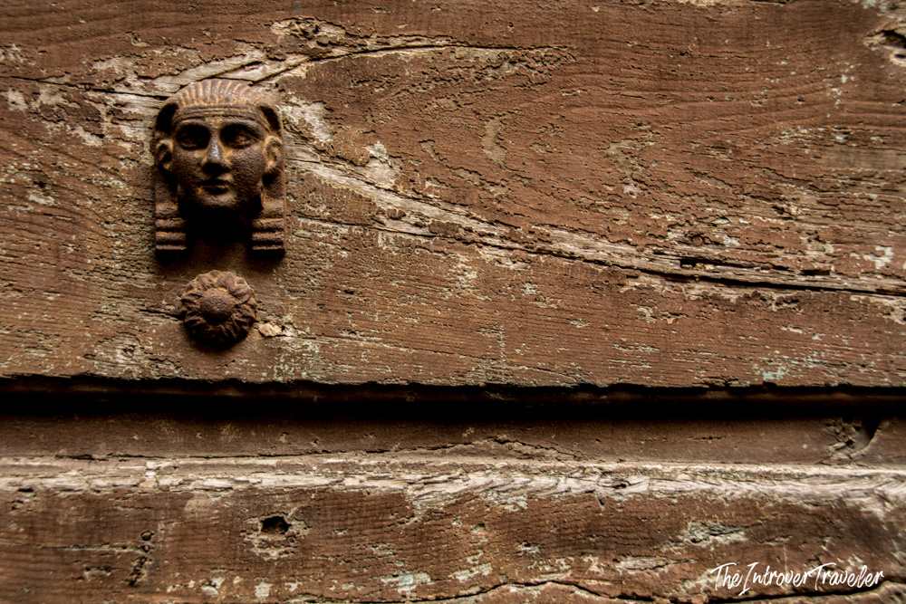 Egyptian-style iron door knocker on a weathered wooden door in Lucca, Tuscany
