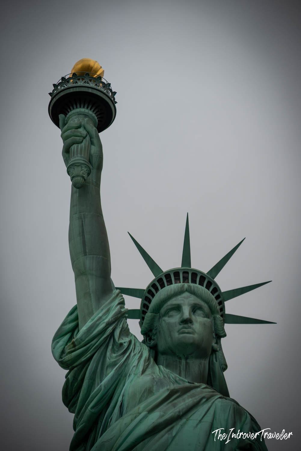 Close-up of the Statue of Liberty crown and golden torch, viewed from Liberty Island on an overcast day