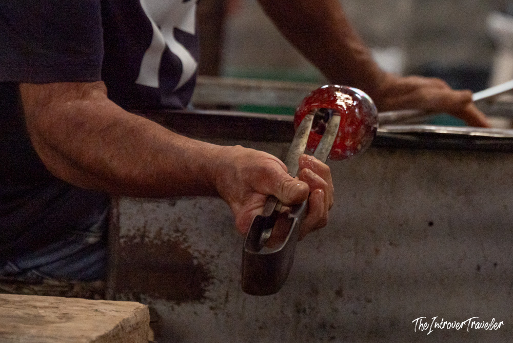 Murano glassmaker shaping hot red molten glass with metal tongs at a Venice furnace workshop