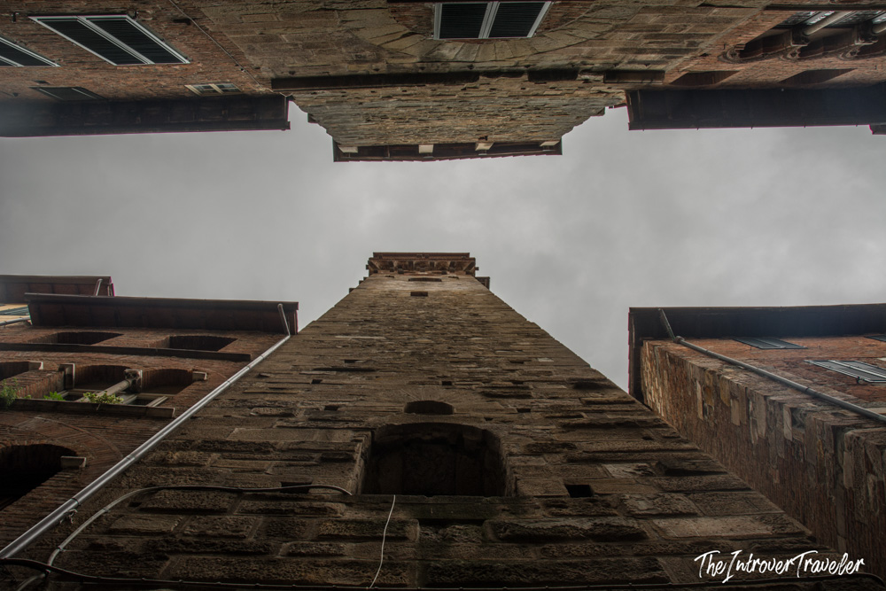 Worm's eye view looking up a medieval tower in Lucca, Tuscany, framed by brick buildings