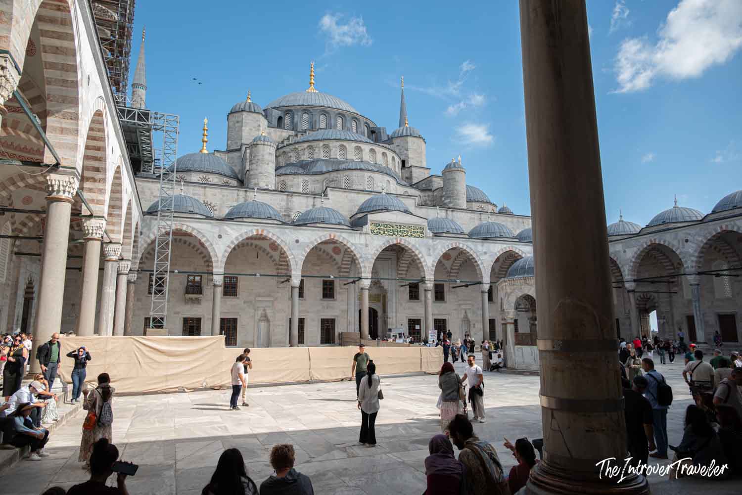 Tourists in the courtyard of the Blue Mosque, Istanbul, with cascading domes and gold finials visible above