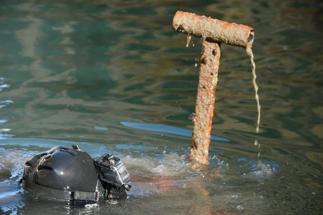 Diver surfacing in a Venice canal holding a rusty metal object recovered from the water