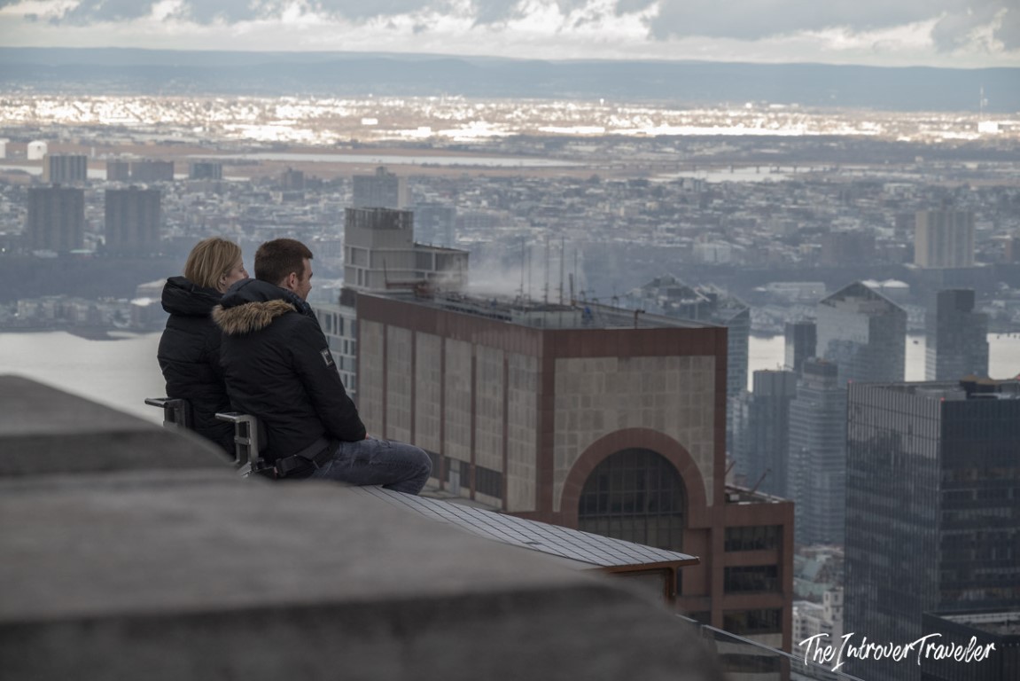 Couple sitting on a bench at Top of the Rock observation deck, overlooking the Manhattan skyline