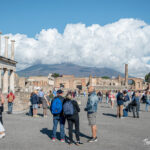 Crowds of tourists exploring the Pompeii Forum with Mount Vesuvius looming in the background