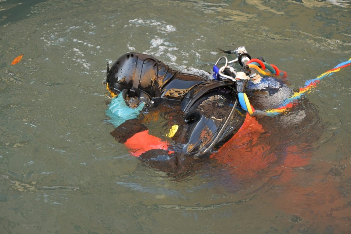 Venice canal diver in wetsuit and helmet surfacing in murky canal water with colorful equipment lines