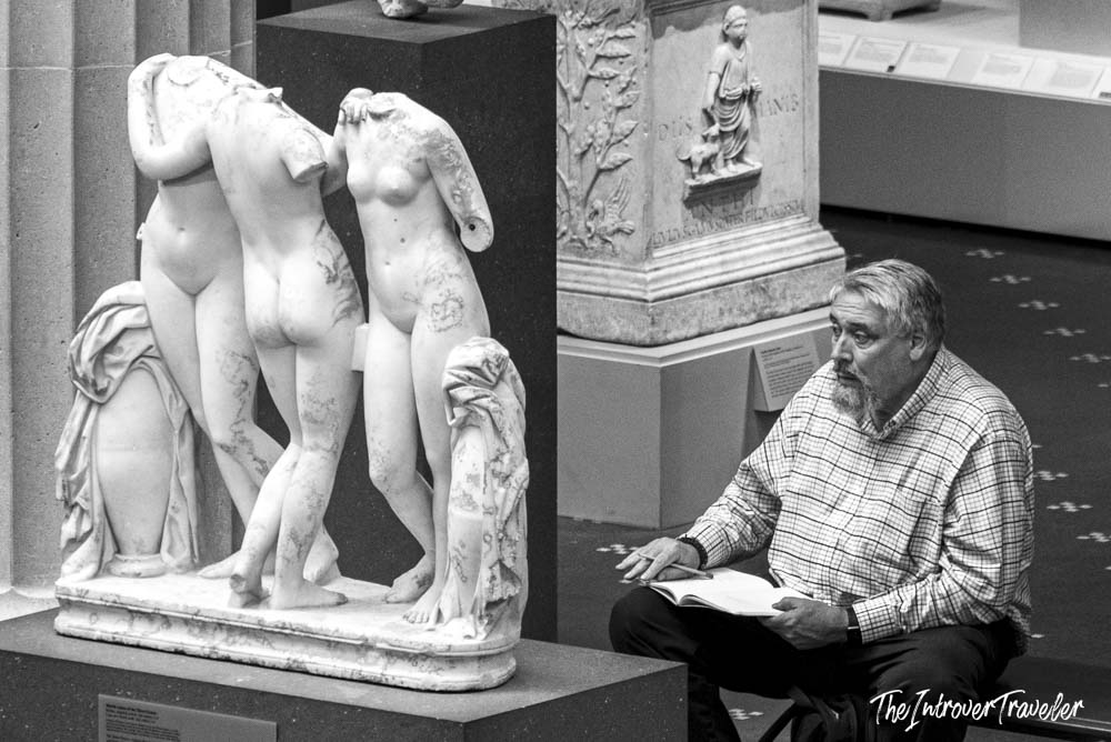 Bearded visitor sketching beside the Three Graces marble sculpture in the Met Greek gallery