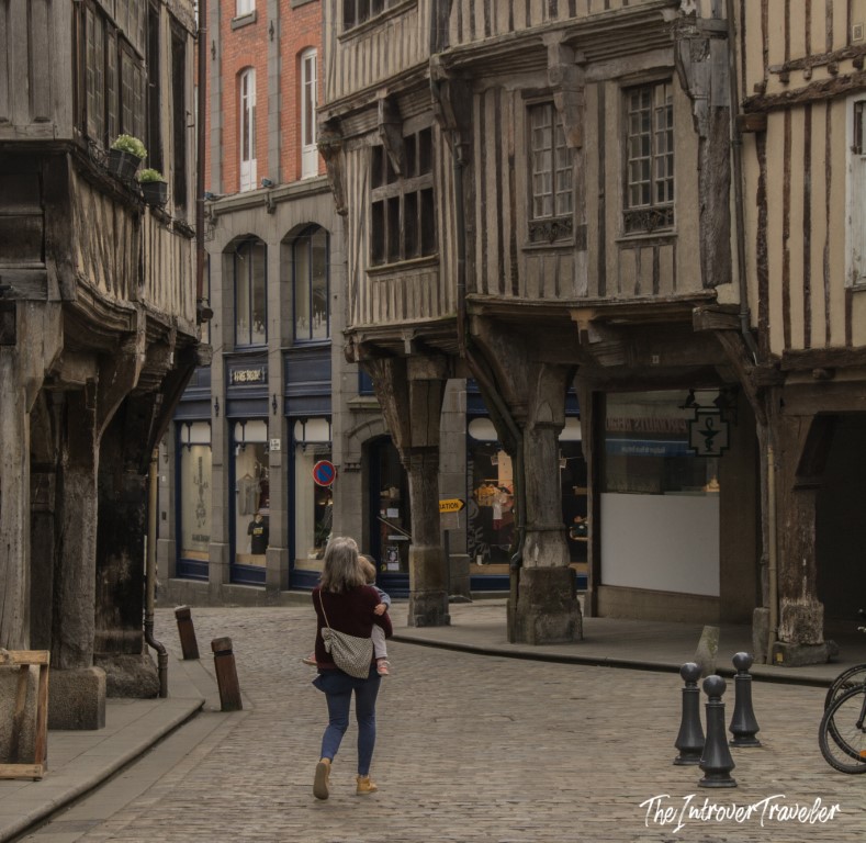 Woman walking a cobblestone street in Dinan, lined with medieval half-timbered buildings on pillars