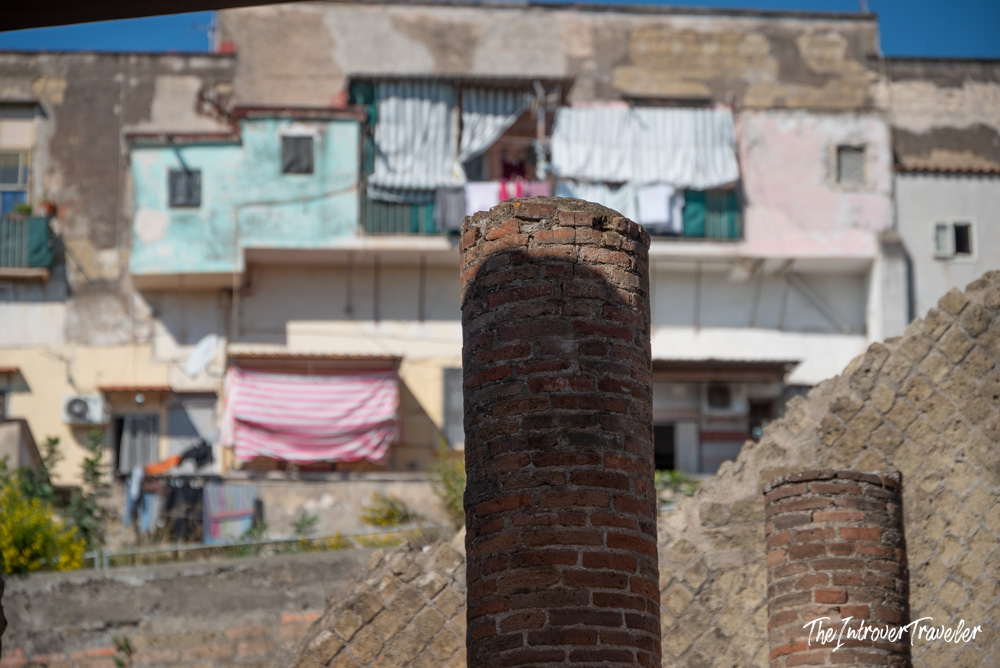 Ancient Roman brick columns at Herculaneum with modern Naples apartments looming above the excavation site