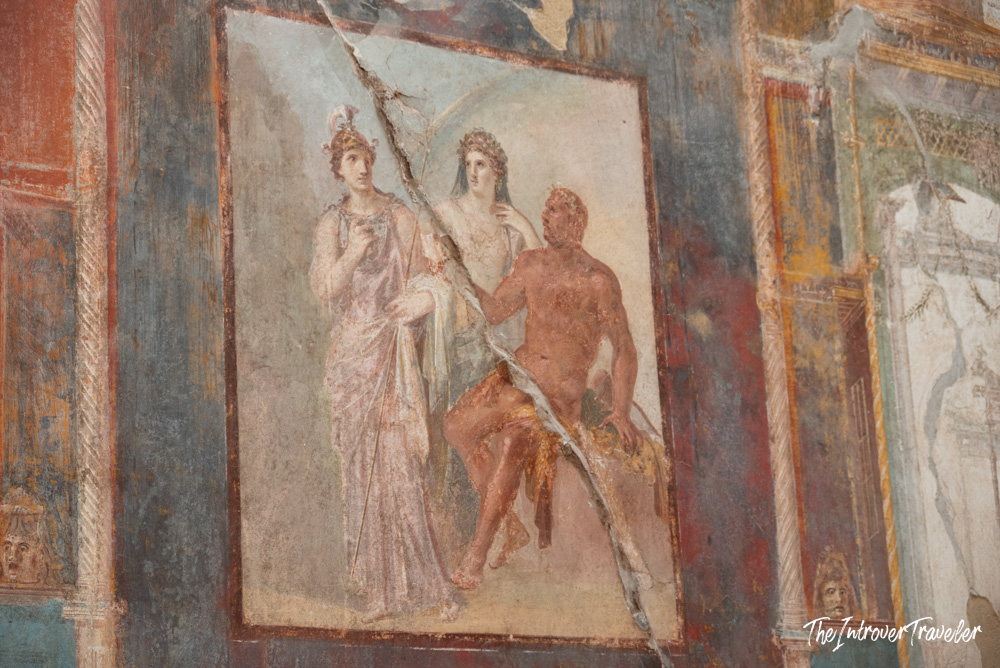 Ancient Roman wall fresco with three mythological figures, preserved inside the Herculaneum excavations