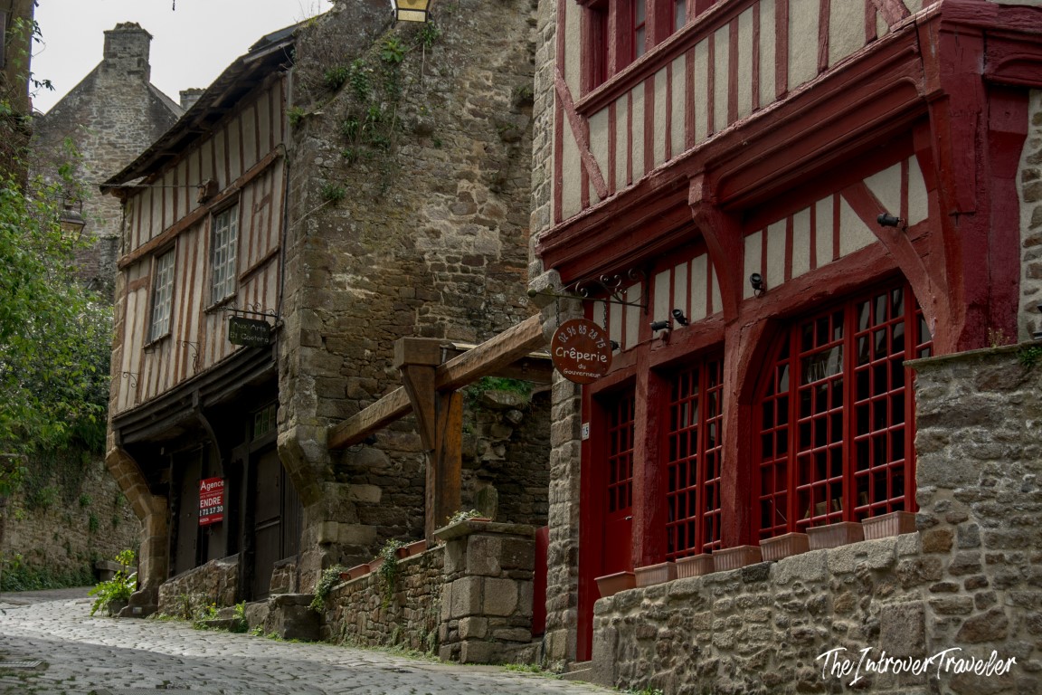 Cobblestone street in Dinan lined with half-timbered buildings and a red Crêperie du Gouverneur