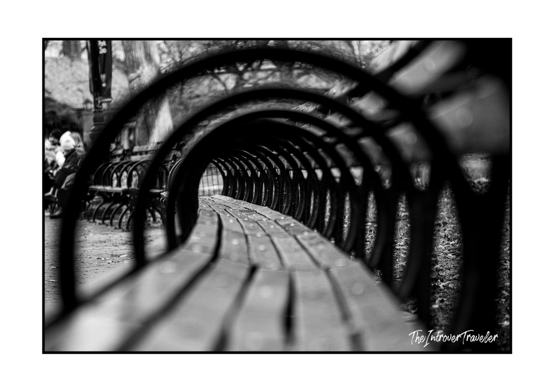 Close-up black and white shot of iconic Central Park bench armrests curving into the distance, New York