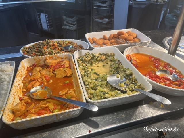 Warm buffet dishes at Plaza Premium Lounge Fiumicino, including chicken stew, vegetables, and fried snacks