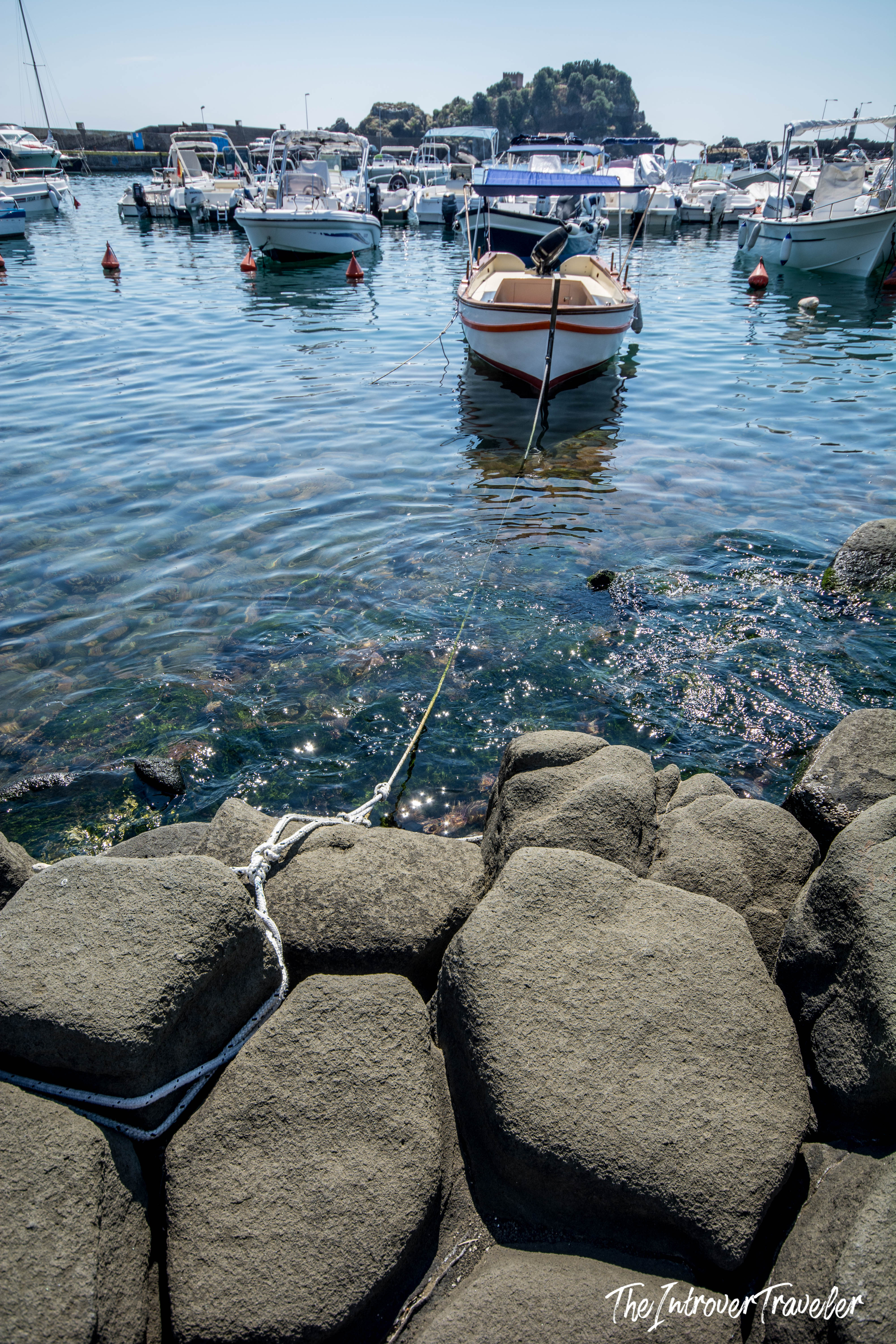 Wooden fishing boat moored at Aci Trezza harbor, tied to volcanic basalt rocks on the Sicilian coast