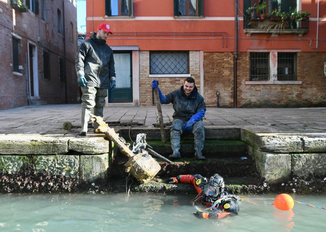 Diver and workers retrieving a submerged engine from a Venice canal beside historic brick buildings