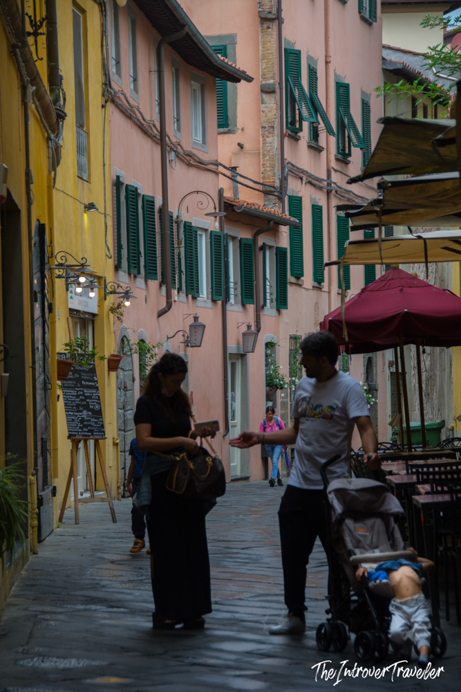 Narrow pedestrian street in Lucca old town with pink buildings and green shutters