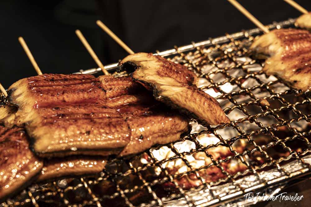 Glazed unagi eel fillets grilling on skewers over charcoal at Nishiki Market, Kyoto