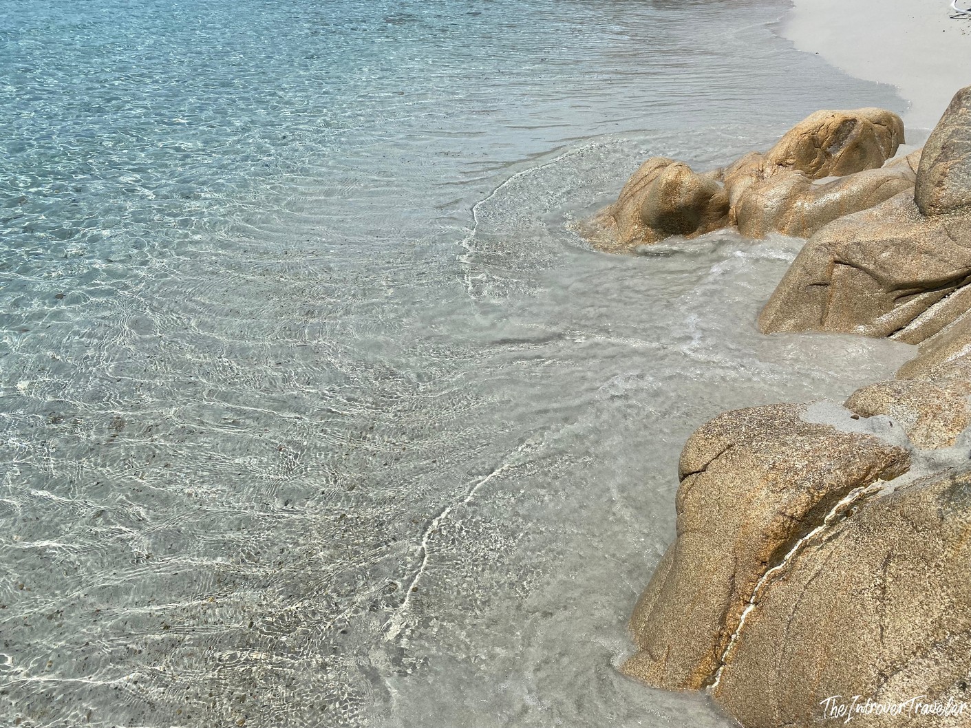 Crystal-clear shallow water lapping granite boulders on a south Sardinia beach