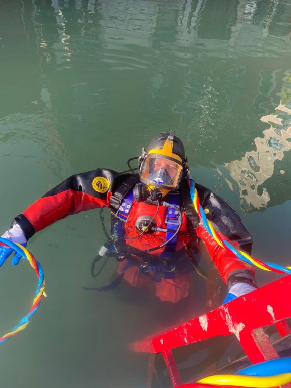 Professional venice canal diver in full diving gear surfacing from murky green canal water