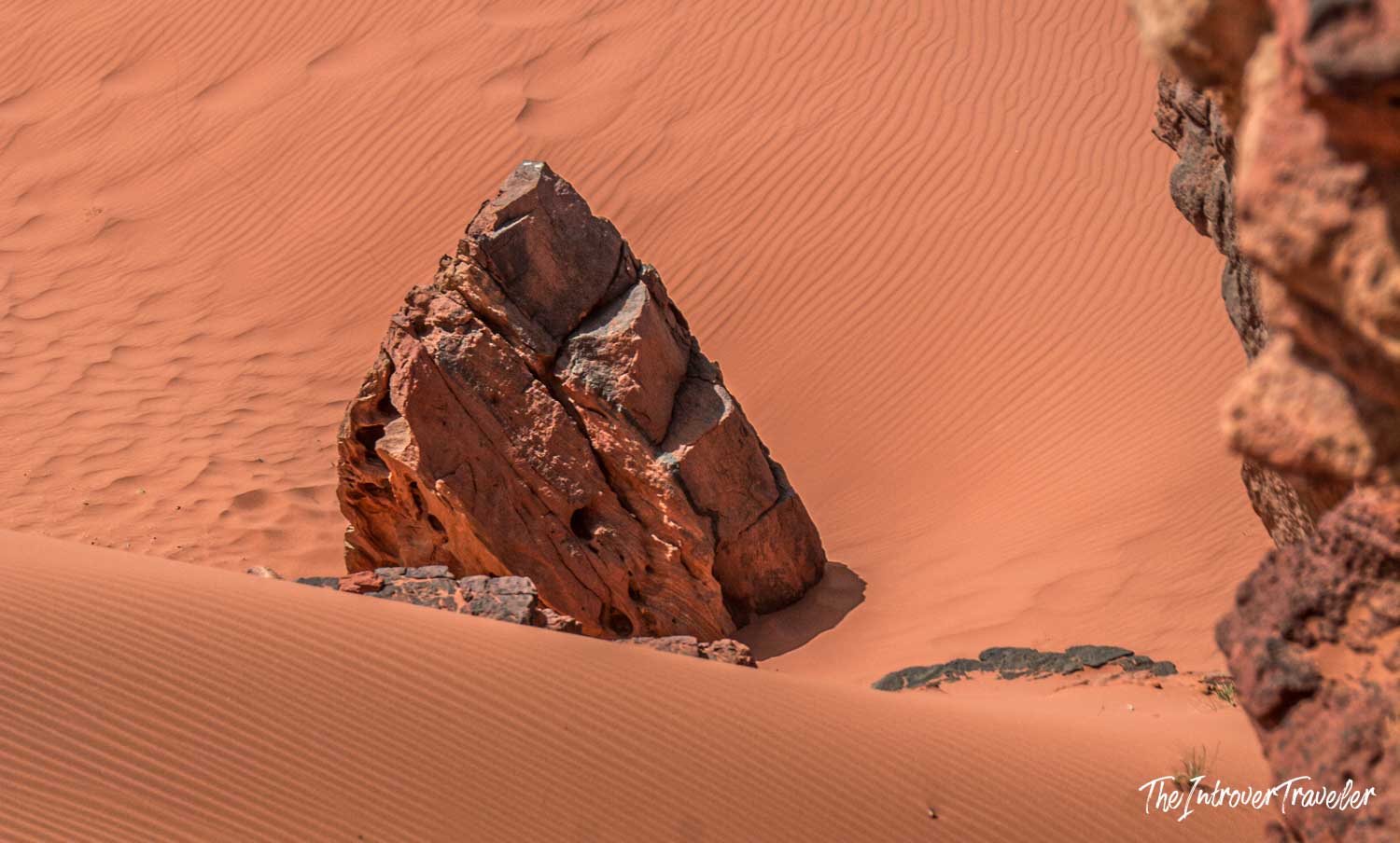 Jagged red rock formation emerging from rippled orange sand dunes in Wadi Rum, Jordan