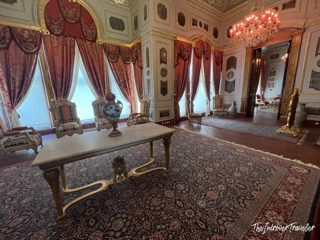 Ornate reception room inside Topkapi Palace, Istanbul, with gilded furniture, red drapes, and a crystal chandelier